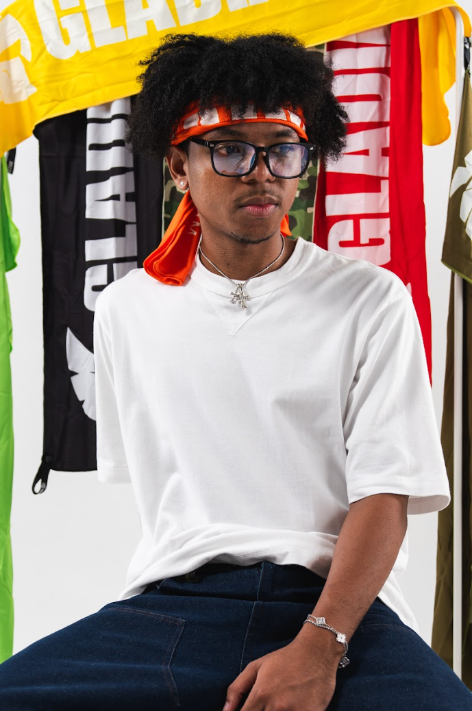 Person wearing a white shirt and dark pants sitting in front of colorful clothing items.